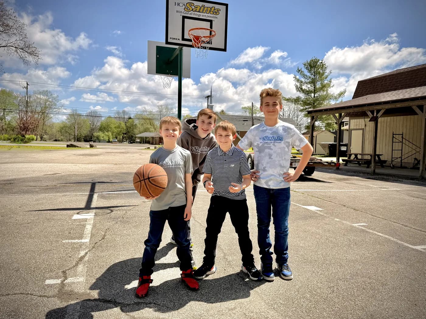Four students with a basketball on the outdoor court on a sunny day, the school building behind them
