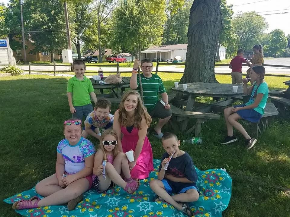 Children sitting on a blanket on the lawn under a tree on a summer afternoon, freeze pops in hand