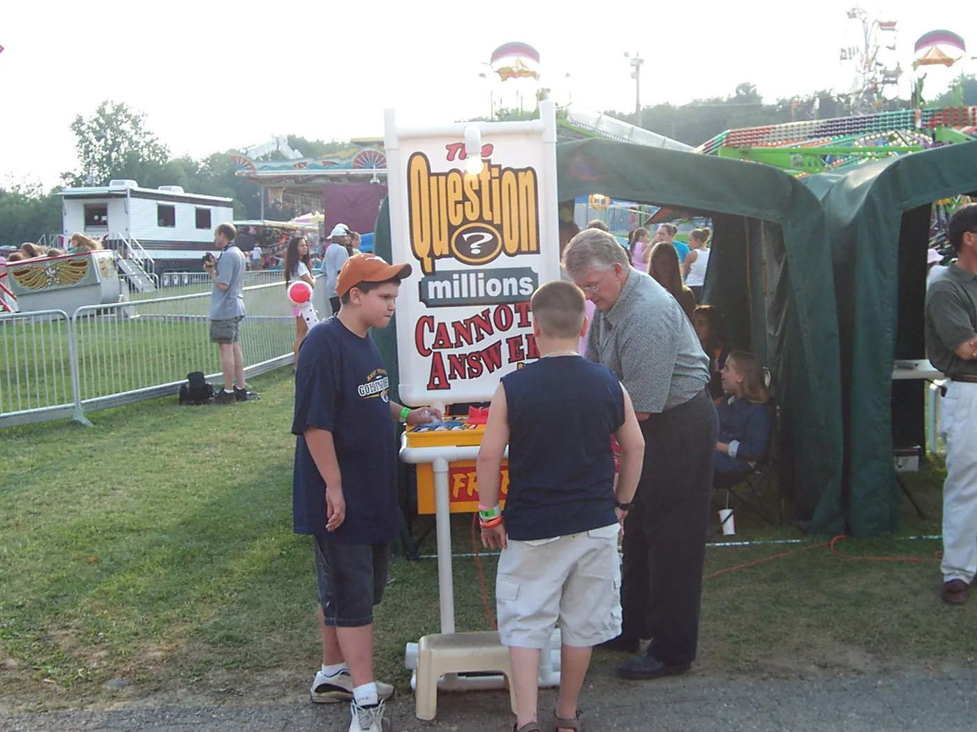 The church’s booth on the fair midway: a tall sign on a stand beside a green tent, with fairgoers gathered around it
