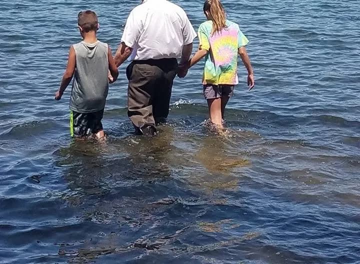A pastor wading into the lake hand in hand with two young people