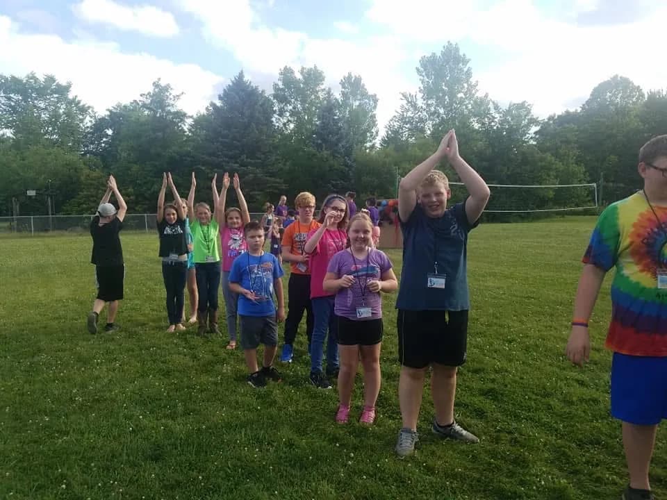 Children and leaders on the field with their arms in the air during a game